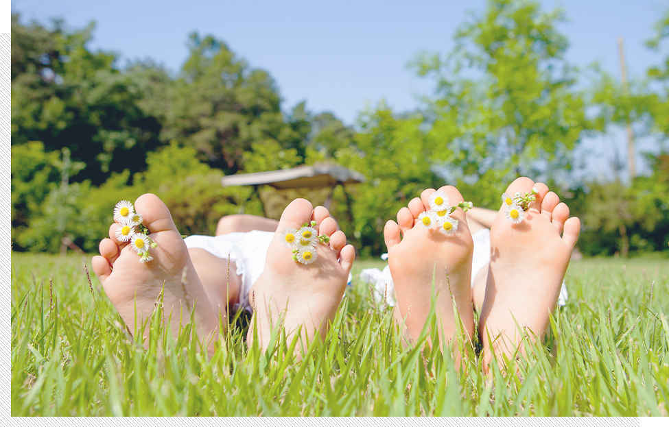 밝은날 풀밭에 누운 두사람이 발바닥에 꽃을 꼽고 발바닥을 보이고 있다